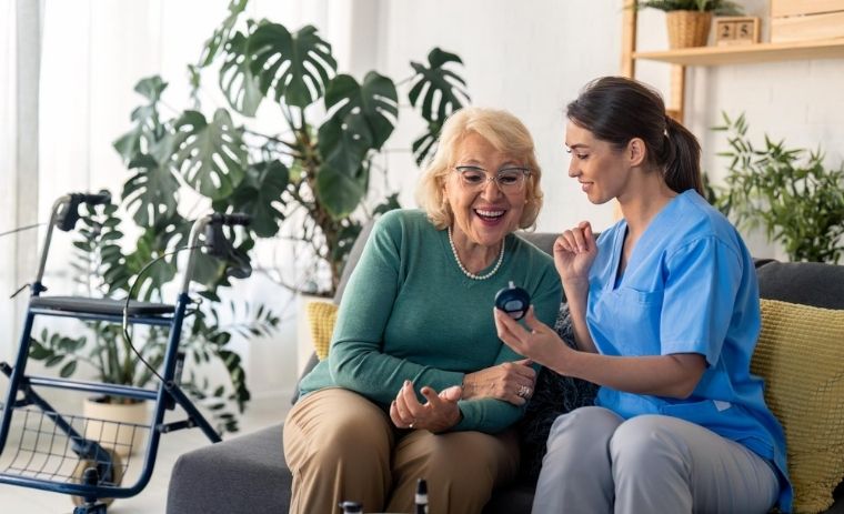 Caregiver providing home health care for seniors in New York, showing medical device to an elderly woman sitting on a sofa at home