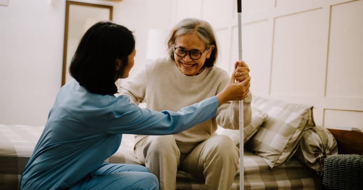 Home health aide assisting an elderly woman with mobility support in her New York home, showing compassionate in-home care and safety.