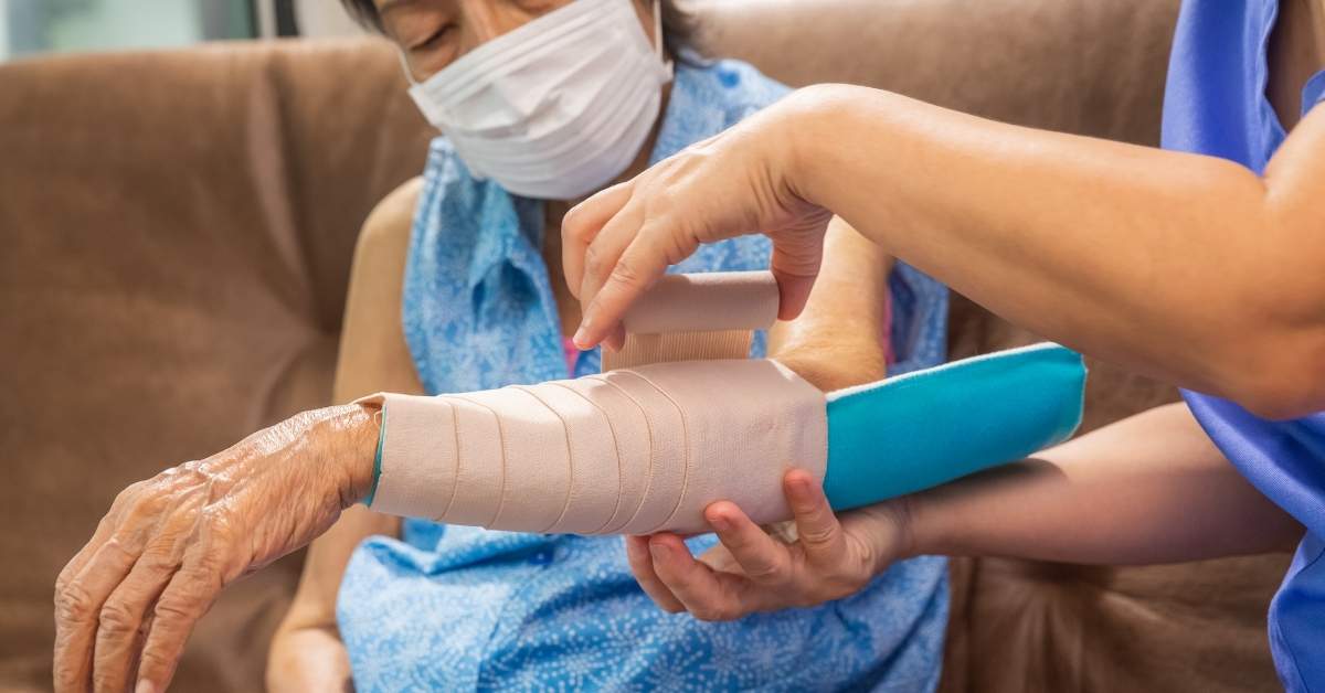 A nurse providing wound care at home for an elderly patient in New York, carefully wrapping the arm to prevent infection safely.