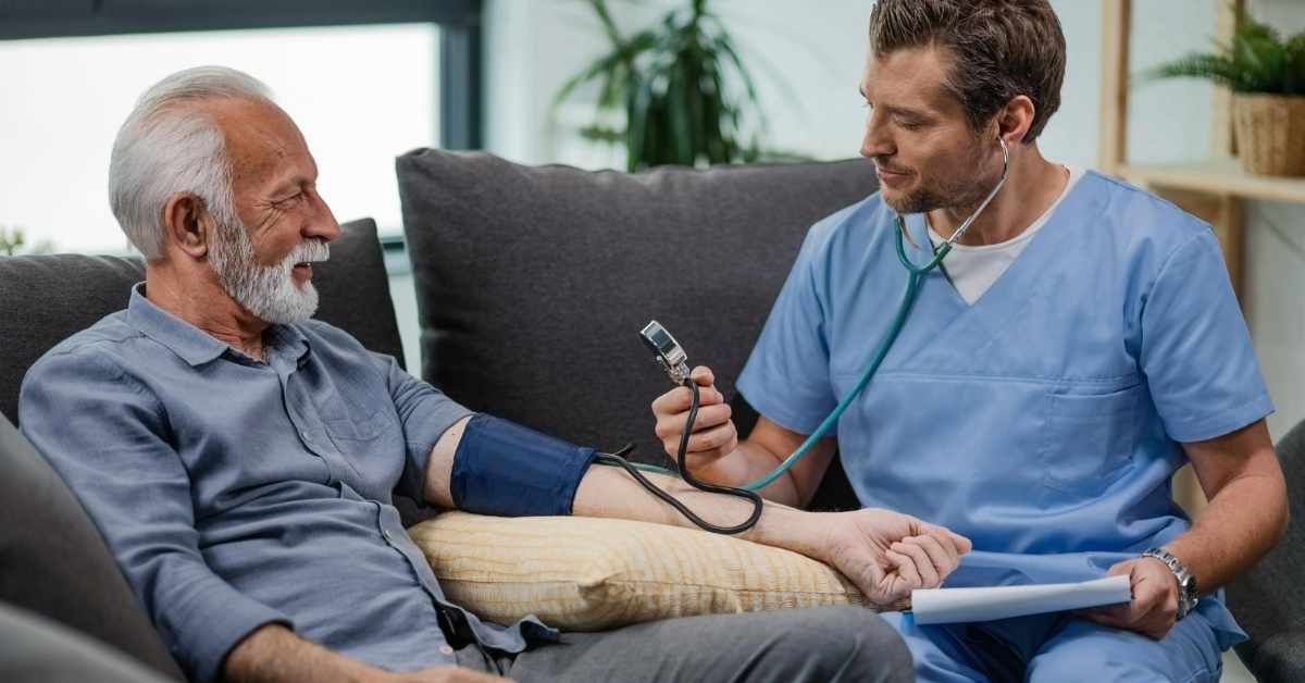 Nurse checking blood pressure of senior man at home, demonstrating medical monitoring at home with professional care.